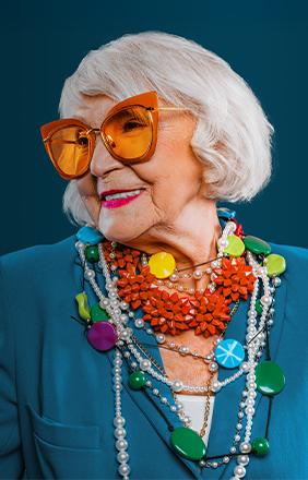 Septuagénaire souriante portant des bijoux colorés et des lunettes de soleil.
