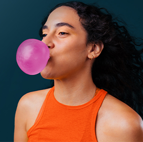 Une personne fait une grosse bulle de chewing-gum rose 