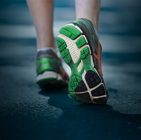 Gros plan d’une personne marchant sur une route, montrant les semelles vertes et noires de ses chaussures de course.