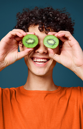 Jeune homme souriant tenant des moitiés de kiwi devant ses yeux.