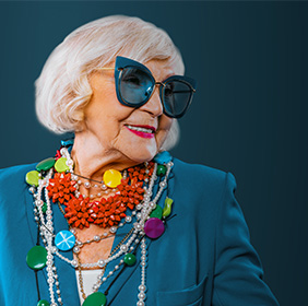 Septuagénaire souriante portant des bijoux colorés et des lunettes de soleil.