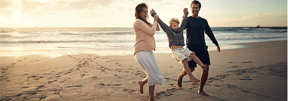 Une famille heureuse marche pieds nus le long d’une plage de sable au coucher du soleil.