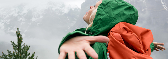 Un randonneur portant une veste verte, les bras écartés, dans un paysage montagneux