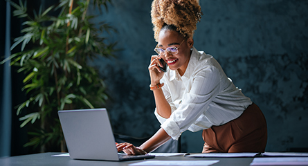 Une femme debout à un bureau utilisant un ordinateur portable et un téléphone.